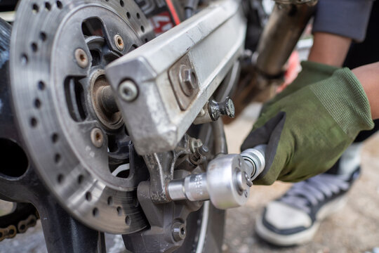 Worker securing motorcycle parts carefully. Focused maintenance on parked motorcycle in urban workshop setting