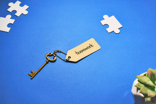 Bronze key attached to a 'teamwork' label, surrounded by disconnected white puzzle pieces on a vibrant blue background.