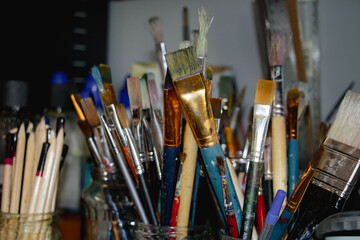 Obraz premium Art paint brushes in a glass jar with colorful paint stains in a cozy creative studio, Close-up of artist tools with soft natural light and selective focus, inspiring artistic workspace