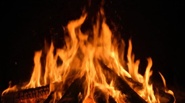 Campfire burning with bright orange flames on logs at night, close up footage for video backdrop.