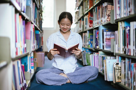 Young Asian Woman Reading Book in Library Corner with Natural Light