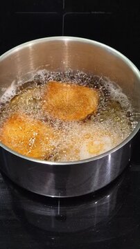 Portuguese rissois being fried in hot oil, a traditional appetizer cooking in a kitchen.