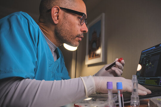 Medical researcher examining blood data on a laptop, holding a test tube
