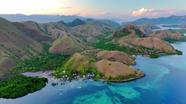 Aerial view of Komodo National Park featuring rolling green hills, lush vegetation, and crystal clear turquoise waters under a soft sunset sky East Nusa Tenggara, Indonesia.