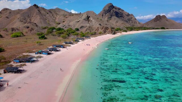 Aerial view of the famous Pink Beach in Komodo National Park with turquoise waters, rugged hills, and small boats along the shore in East Nusa Tenggara, Indonesia.