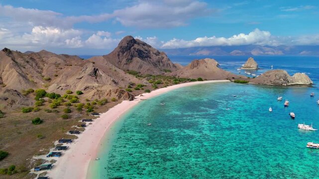 Aerial view of the famous Pink Beach with turquoise waters, coral reefs, and volcanic hills under a blue sky in Komodo National Park, East Nusa Tenggara, Indonesia.