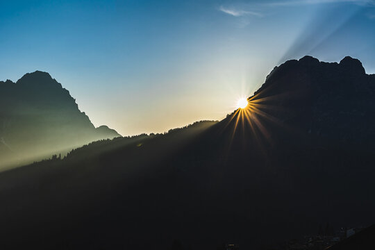 sole che tramonta dietro alle montagne, sagome scure delle catene montuose che vengono messe in risalto dalla luce del sole in un cielo sereno