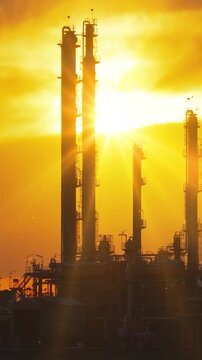 Cinematic aerial view of a petrochemical plant at sunset. Industrial towers, pipelines, and refinery structures stand against a glowing orange sky as warm sunlight reflects across the facility