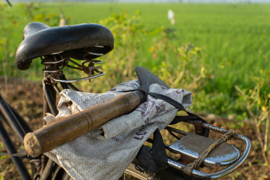 Close-up of a traditional sickle on a vintage bicycle rack with a blurred green field background.