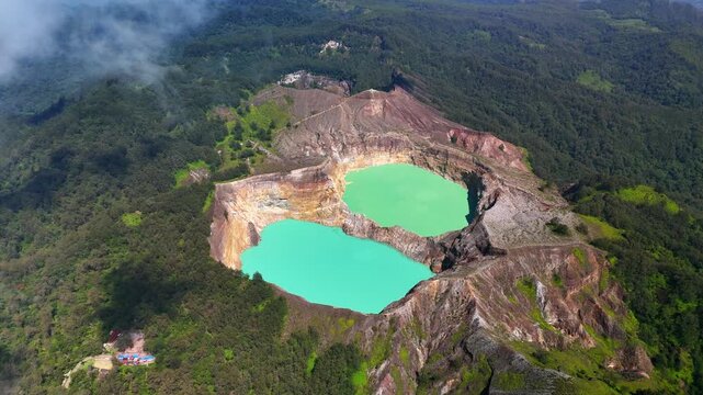Aerial view of Kelimutu National Park featuring the vibrant turquoise and green crater lakes surrounded by steep rocky cliffs and lush tropical forests in Detusoko, East Nusa Tenggara, Indonesia.