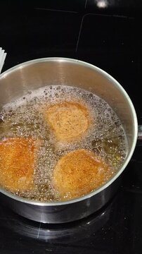 Portuguese rissois being fried in hot oil, a traditional appetizer cooking in a kitchen.