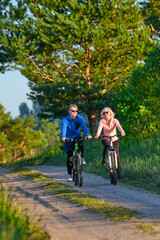 Obraz premium Active man and woman cycling on dirt road through sunny forest
