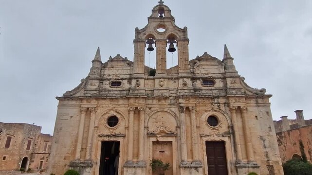 Walking to Arkadi Monastery entrance in Rethymno, Crete. 4k video of Venetian facade and dark interior with burning candles accent. Ancient Orthodox church atmosphere with flickering lights, no people
