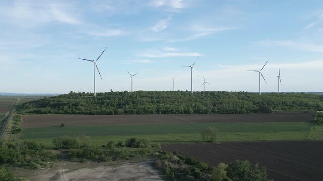 Aerial rising shot revealing multiple wind generators producing clean energy in a natural landscape.