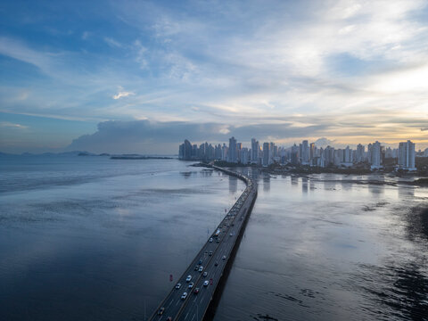 Panama city skyline standing majestically along the coastline with the corredor sur highway buzzing with cars and traffic during a serene sunset - stock photo