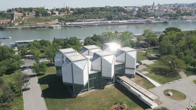 Sharp edges and triangular concrete patterns of brutalist socialist era building in New Belgrade, Serbia. Drone video with river and old town panorama behind.