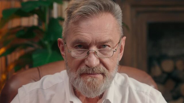 Portrait in office old senior Caucasian business man serious looking at camera in workplace retired aged businessman look calm confident face gaze wisdom elderly gray haired male in glasses close up