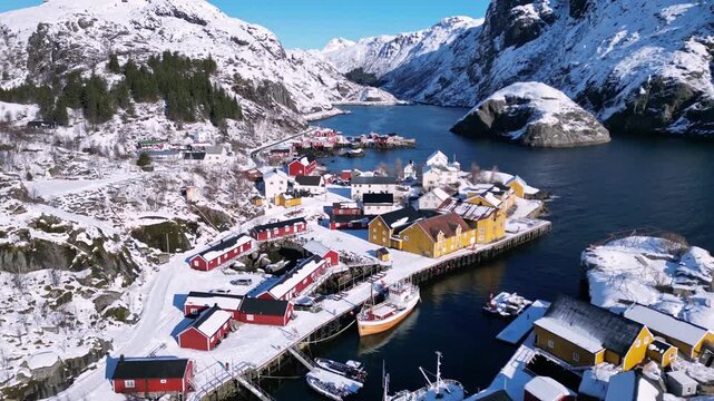 Aerial view of the historic fishing village of Lofoten with red and yellow cabins nestled among snowy mountains and calm fjord waters Nordland, Norway.