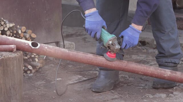 A dedicated worker uses an electric angle grinder to smooth a rusty metal pipe, showcasing vital industrial repair skills and essential maintenance tasks within a busy workshop area