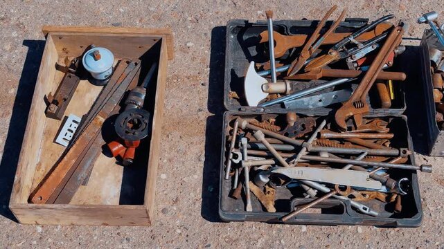 Rusty tools in boxes on asphalt, summer street flea market scene showing assorted vintage hand tools, saw, wrenches, hammers