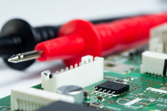 Close-up of a circuit board with electronic components and a multimeter with test probes.