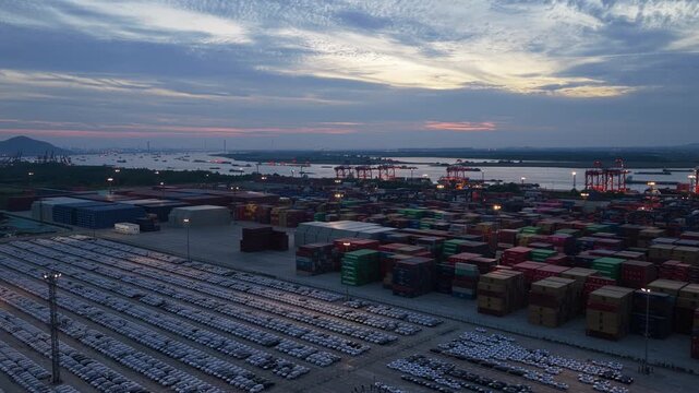 Aerial panorama of container stacks and car storage yard at coastal port during dusk