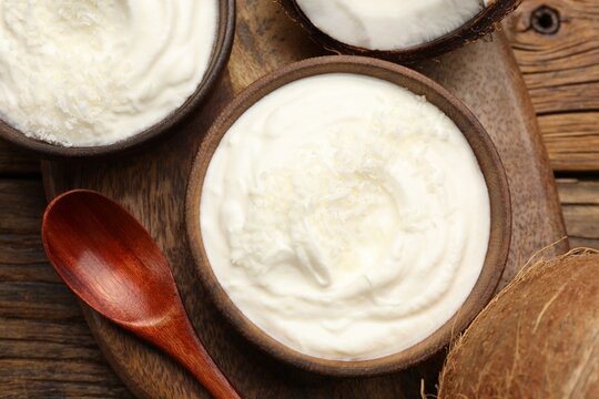 Tasty coconut yogurt with flakes on wooden table, flat lay