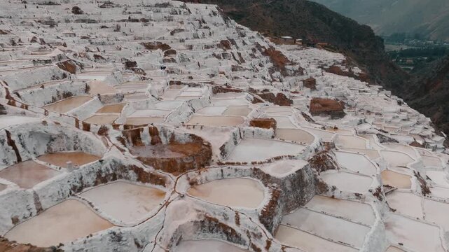Drone aerial view of the historic Maras Salt Mines near Cusco, Peru. Thousands of terraced salt evaporation ponds cover the mountainside, creating a striking geometric pattern in the heart of the Sacr