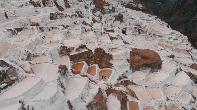 Drone aerial view of the historic Maras Salt Mines near Cusco, Peru. Thousands of terraced salt evaporation ponds cover the mountainside, creating a striking geometric pattern in the heart of the Sacr