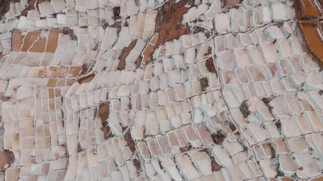 Drone aerial view of the historic Maras Salt Mines near Cusco, Peru. Thousands of terraced salt evaporation ponds cover the mountainside, creating a striking geometric pattern in the heart of the Sacr