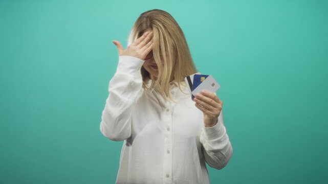Woman holding creditcards in right hand and touching forehead with left hand in studio; financial frustration.