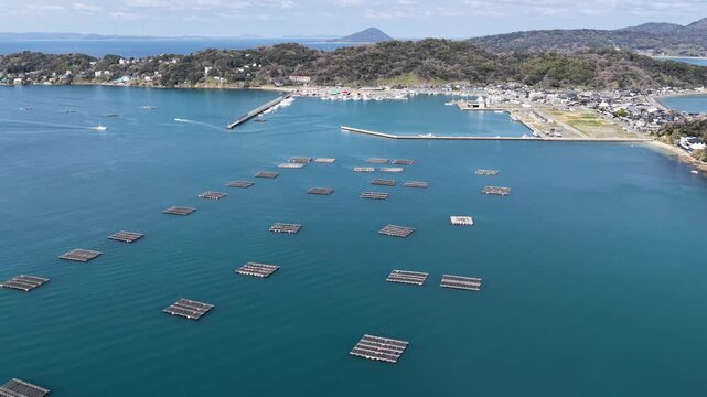 Aerial view of oyster farming rafts floating in the calm blue waters of the bay near the coastline of Itoshima Peninsula, Itoshima, Fukuoka, Japan.
