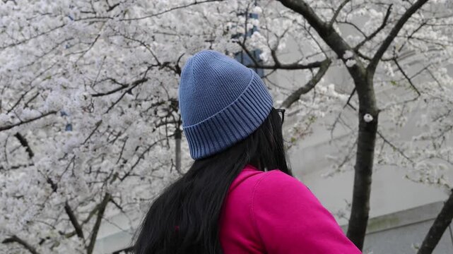 woman in woven knit winter hat looking at spring blooming cherry blossoms sign of season changing close up brunette young lady sweater springtime seasons change