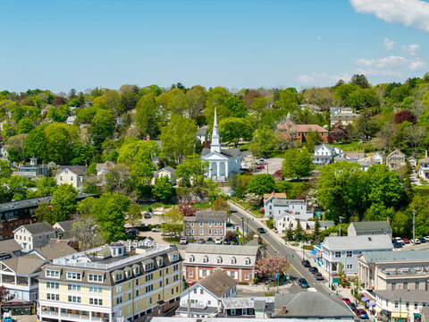 Mystic historic town center, a scenic high-angle view looking down West Main Street toward the iconic white steeple of the Mystic Congregational Church nestled in green trees in Mystic, Connecticut.