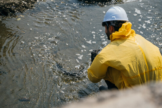 Scientist in a yellow hazmat suit collecting water samples from a polluted coastal stream to conduct a thorough environmental safety and chemical hazard investigation