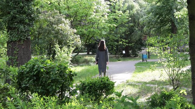 Woman walking alone on a sunny path through a lush green park in summer