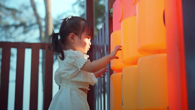 Curious little Asian toddler girl playing with large Tic-Tac-Toe game blocks at an outdoor playground during golden hour. Concentrated child learning through play in a park at sunset. Concept of early