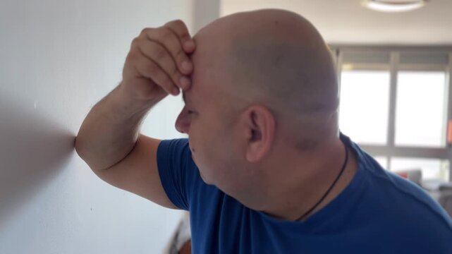 Hombre muy preocupado apoyado en la pared toc&aacute;ndose la cara