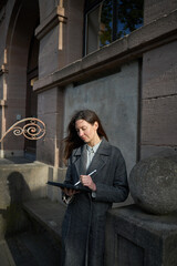 Obraz premium Woman using a stylus on a tablet device while leaning against a stone wall outdoors