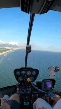POV from a helicopter cockpit of an adult man pilot and passenger flying above the coastline of Barra da Tijuca, Rio de Janeiro, Brazil.