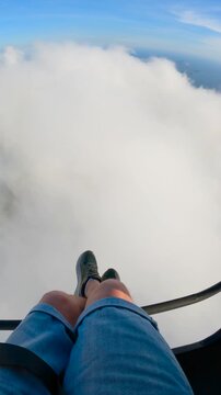 POV view of a man's legs and feet dangling over a thick layer of clouds during a paragliding flight in Rio de Janeiro, Brazil.