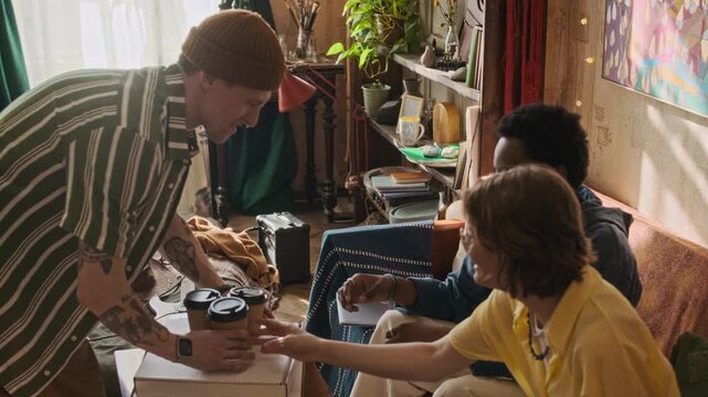 Tracking handheld shot of diverse roommates drinking coffee and eating ordered pizza while gathering during leisure time