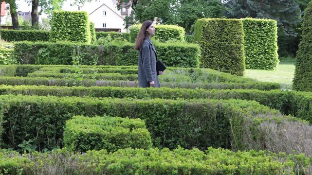 Woman walking through a meticulously manicured hedge maze garden on a sunny day
