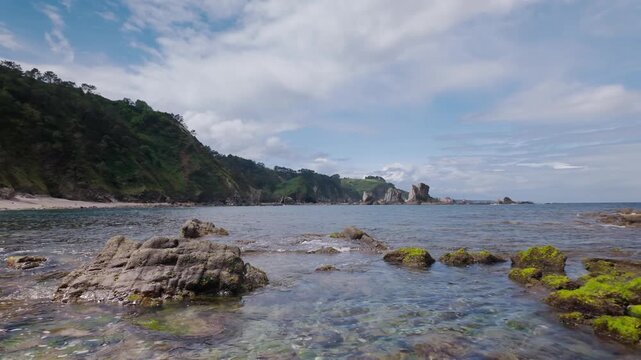 Aerial footage moving backwards over the clear waters of the Cantabrian Sea, revealing the stunning cliffs and unique rock formations of the famous Playa del Silencio in Asturias, Spain