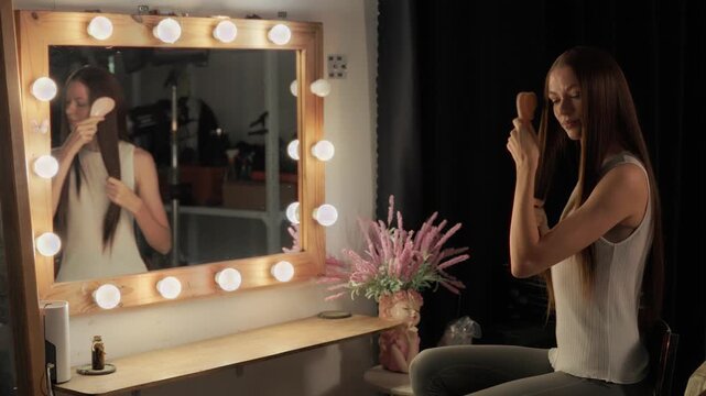 A woman with long brown hair combing her hair while looking in the mirror