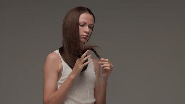 Dark-haired woman examines the ends of her hair.