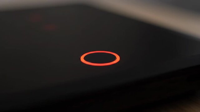 Close-up of a black device with a glowing red circular button in the center. Abstract