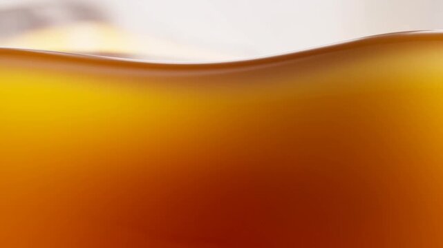 Slow motion tracking shot of amber liquid surface rippling and flowing inside glass container in studio close up