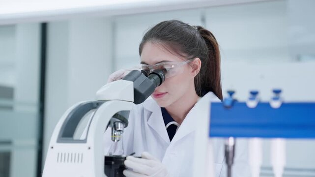 A scientist looks through a microscope to analyze samples in a laboratory. The walls are bright and the equipment is new. The focus is on research and findings.