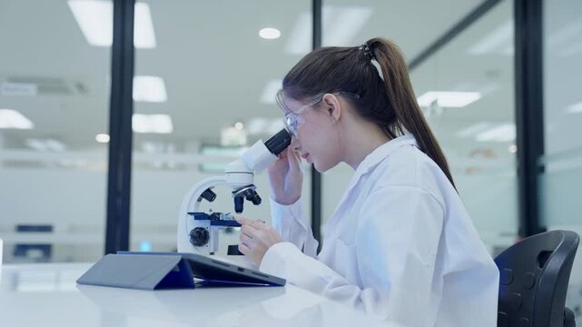 A scientist looks through a microscope to analyze samples in a laboratory. The walls are bright and the equipment is new. The focus is on research and findings.